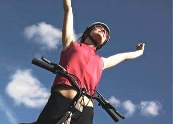 woman standing at her bike with arms raised in victory